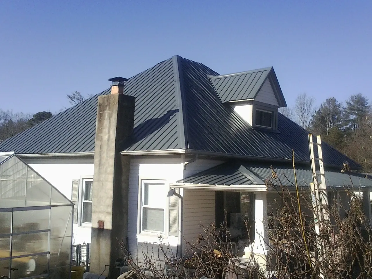Dark blue standing seam metal roof on a white farmhouse with dormer — Slate & Tile Roof Repair by Roofing Brothers in Oelwein