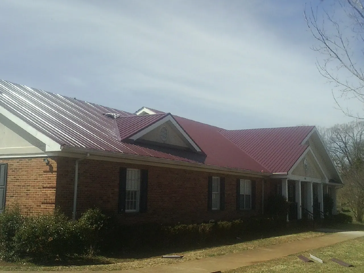 Red metal roof with gabled entries on a long brick building, from a Hail Damage Roof Repair job in Oelwein