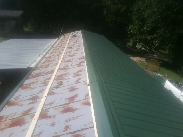 Old rusted panels beside newly installed green metal roofing — Wind Damage Roof Repair by Roofing Brothers in Oelwein