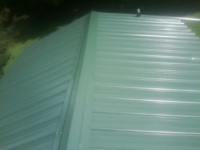 New green metal panels meeting at the ridge of a roof — Flat Roof Repair work by our crew in Oelwein