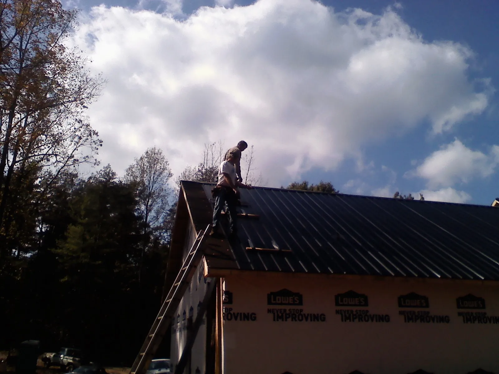 Roofer fastening dark metal panels high against a cloudy sky, from a Roof Inspection job in Oelwein