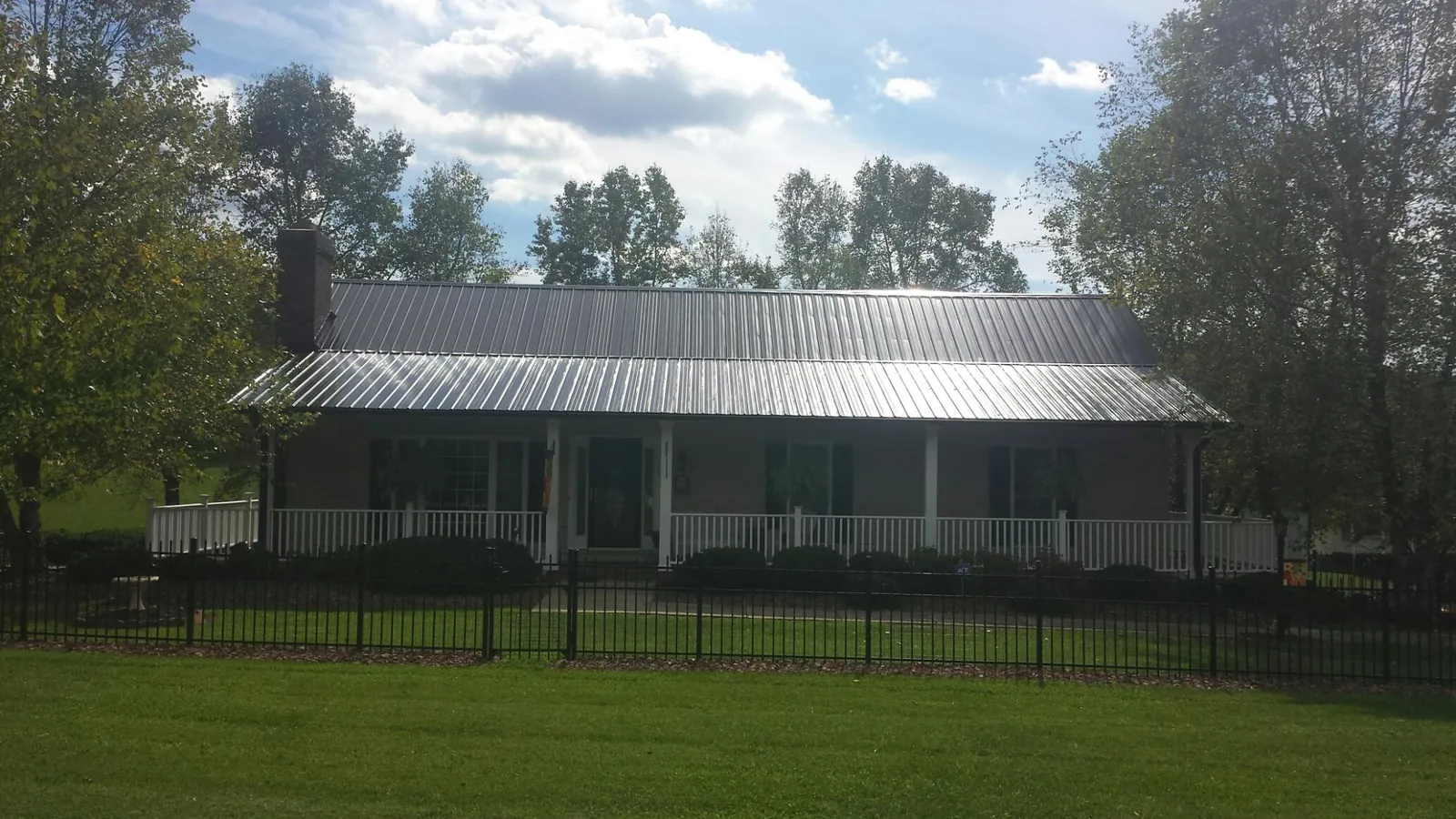 Gray metal roof on a brick ranch with a full width front porch — Gutter Guard Installation work by our crew in Oelwein