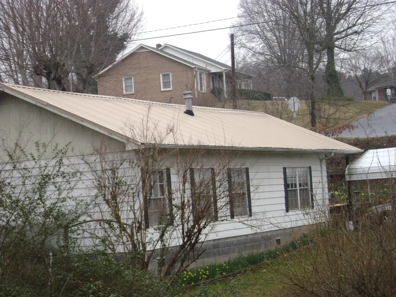 Tan metal roof on a white sided house set into a hillside — Commercial Roofing by Roofing Brothers in Oelwein