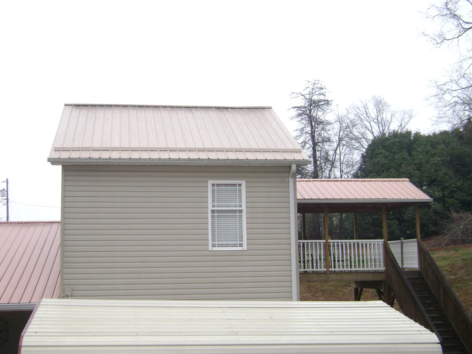 Tan metal roofs on a two story addition and attached porch, from a Roof Replacement job in Oelwein