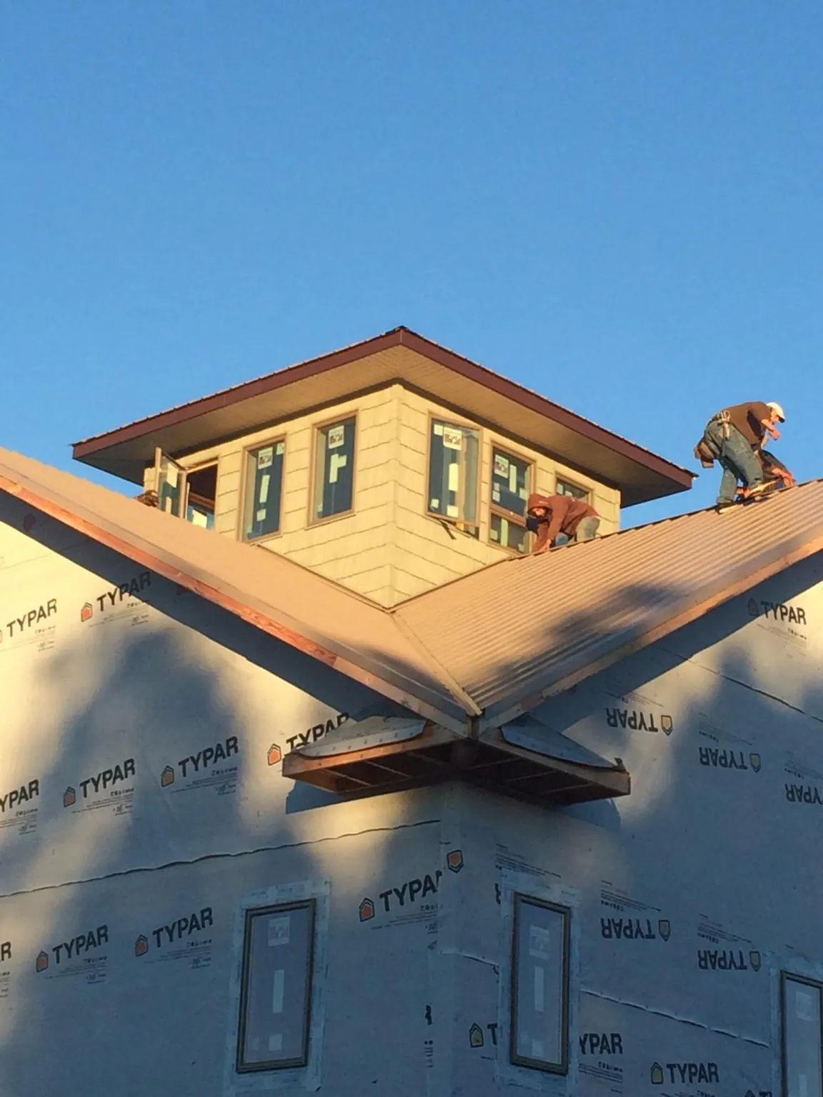 Roofers working around a rooftop cupola on a new metal roof at sunset — Roof Waterproofing in Oelwein by Roofing Brothers